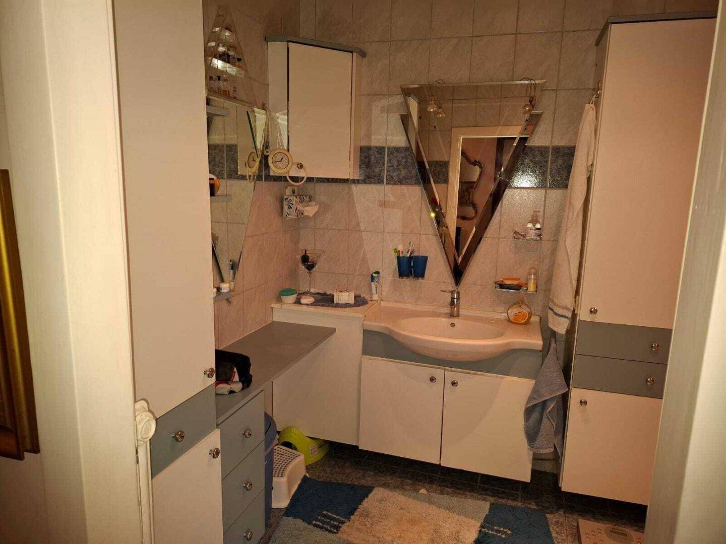 Badezimmer mit Waschbecken, Spiegelschrank und Fliesen, das einen älteren Stil aufweist und Renovierung benötigt.