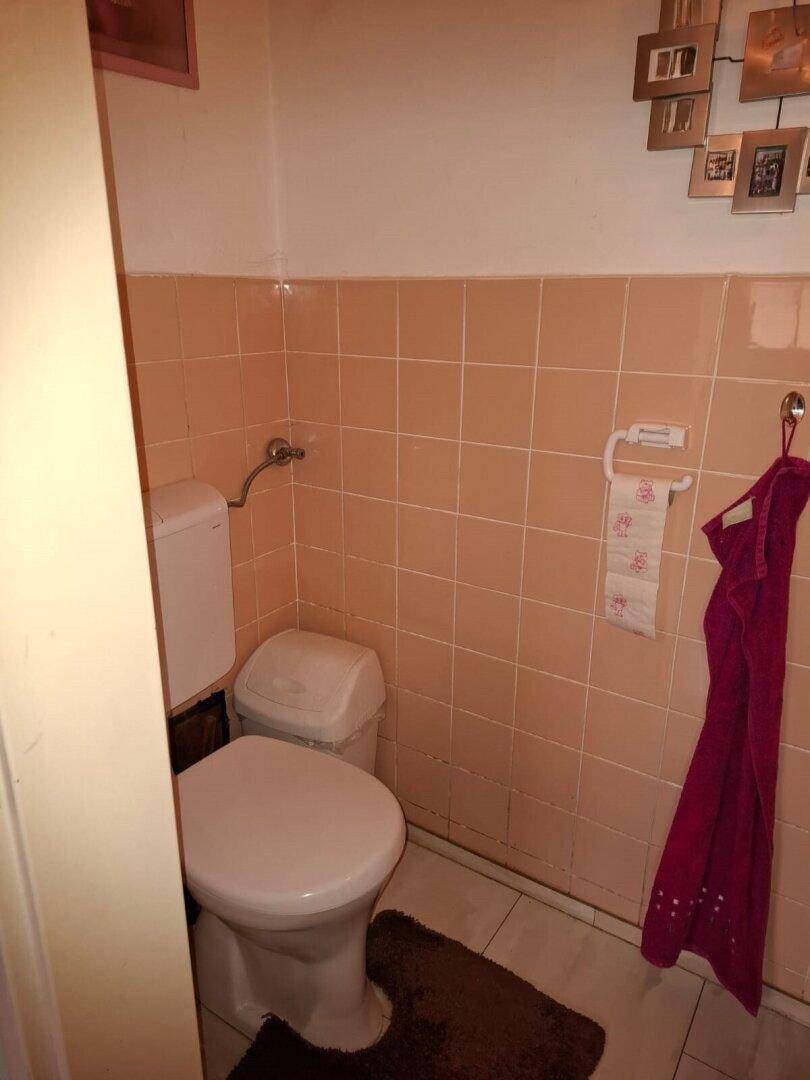 Separate Toilette mit Fliesen in Pastellfarben, die einen älteren, aber funktionalen Zustand zeigt.
