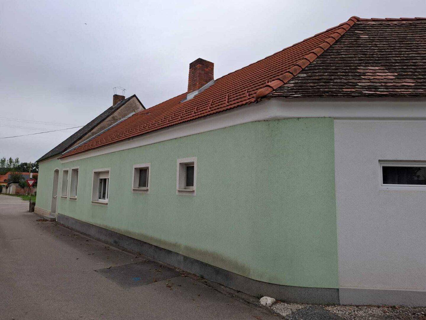 Seitenansicht des Gebäudes mit Ziegeldach und hellgrüner Fassade, die sich in die Umgebung einfügt.