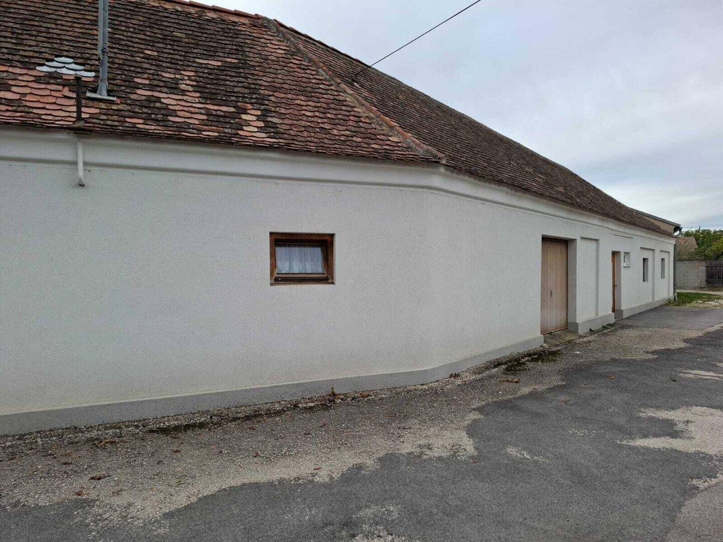 Seitenansicht des Gebäudes mit weißer Fassade und Ziegeldach, das einen ländlichen Charme besitzt und älter ist.