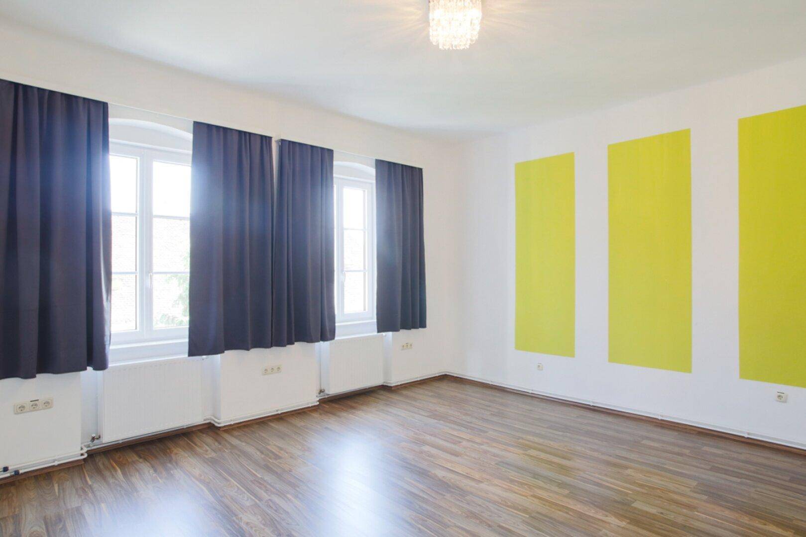 Geräumiges Zimmer mit Holzfußboden und auffälligen grünen Wandpaneelen.