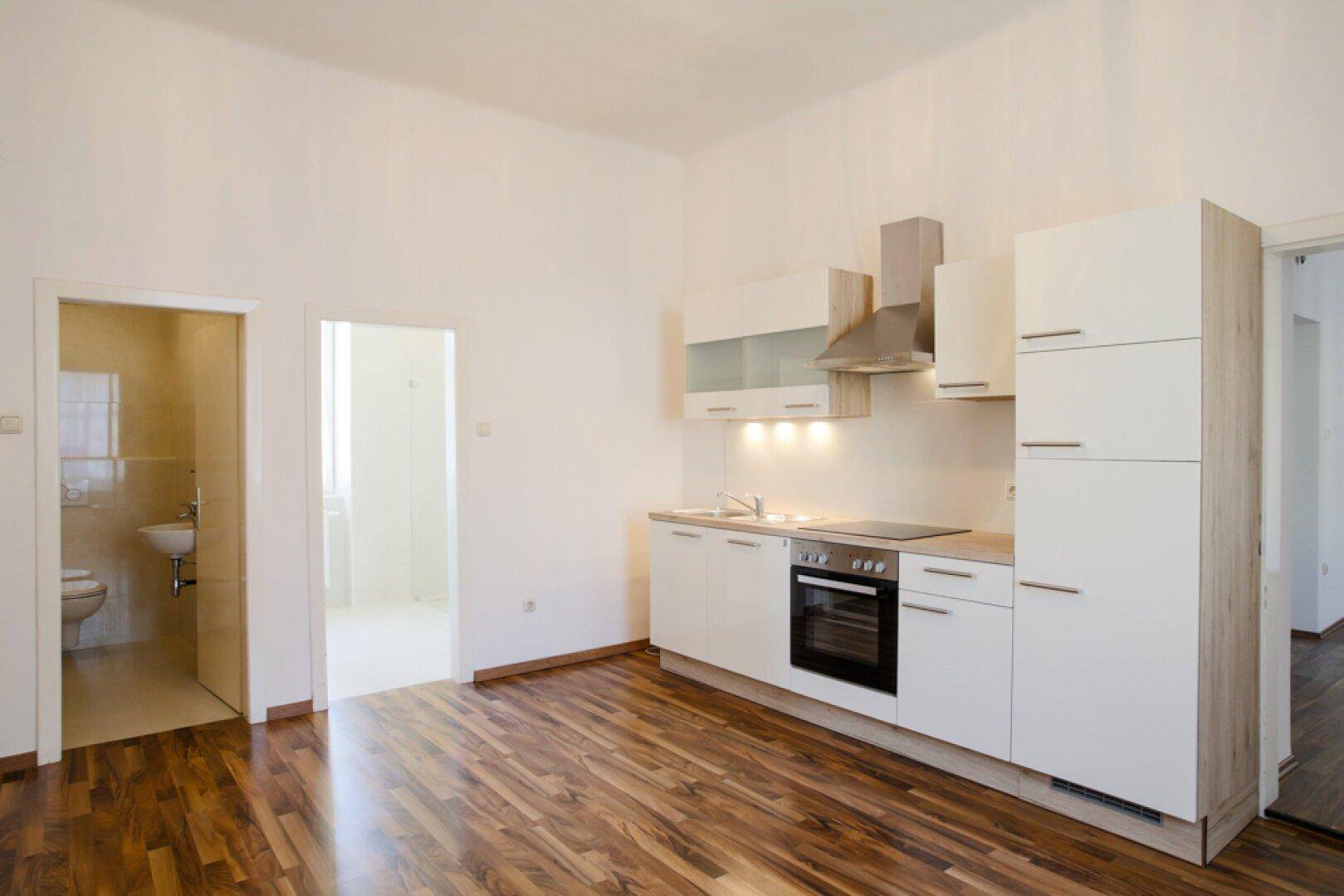 Moderne Einbauküche mit weißen Schränken, Ofen und Dunstabzugshaube, angrenzend an ein WC.