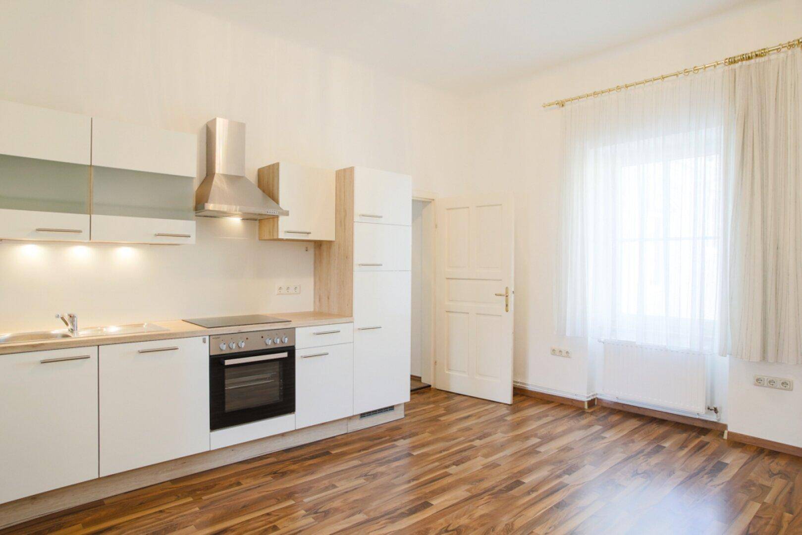 Helle Küche mit weißen Einbauschränken, Holztheke und Fenster mit transparenten Vorhängen.