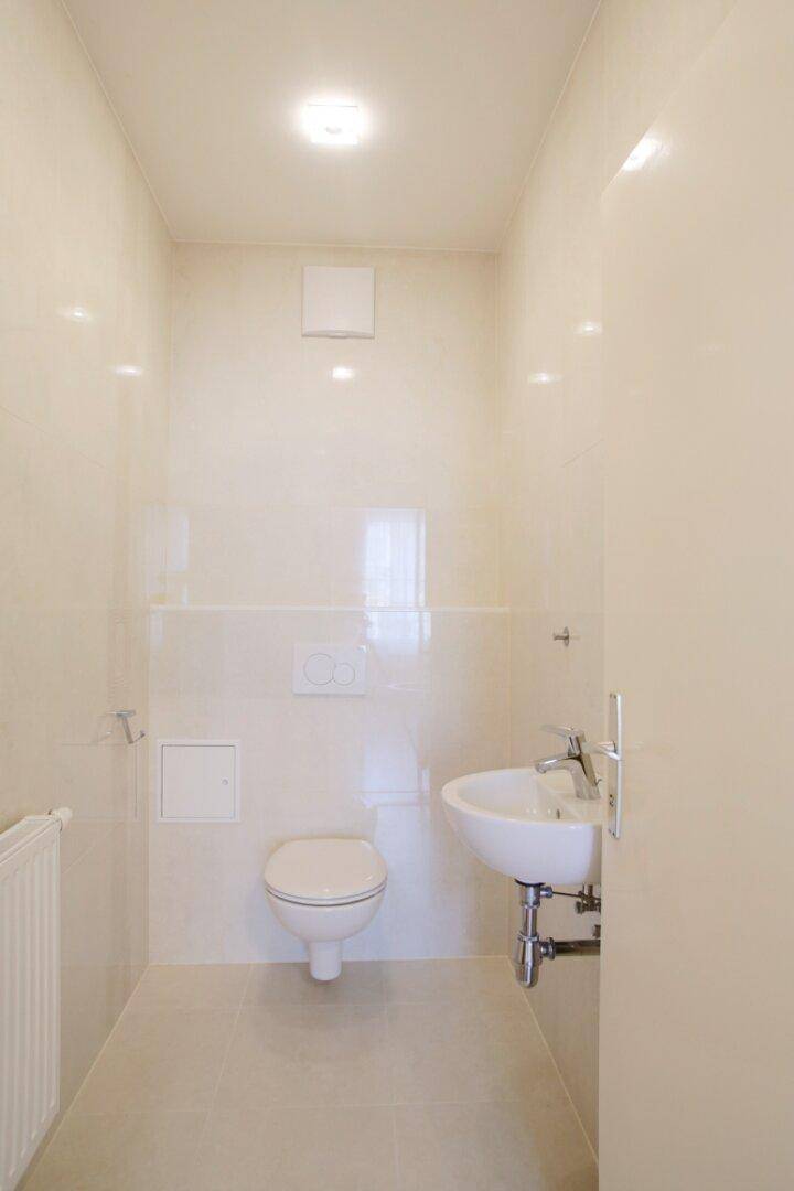 Kleines, hell gefliestes WC mit wandhängender Toilette und Einzelwaschbecken.