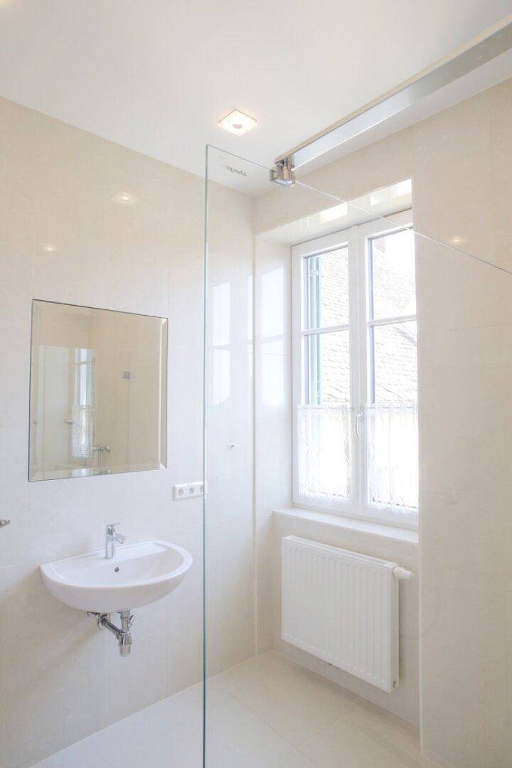 Modernes Badezimmer mit Fenster, Einzelwaschbecken, Spiegel und Duschabtrennung aus Glas.