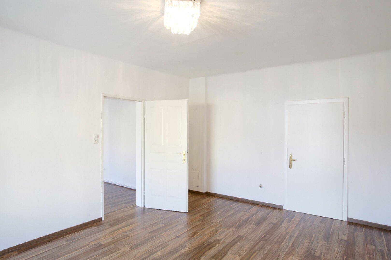 Geräumiges Zimmer mit Holzfußboden und mehreren weißen Türen, die zu anderen Räumen führen.