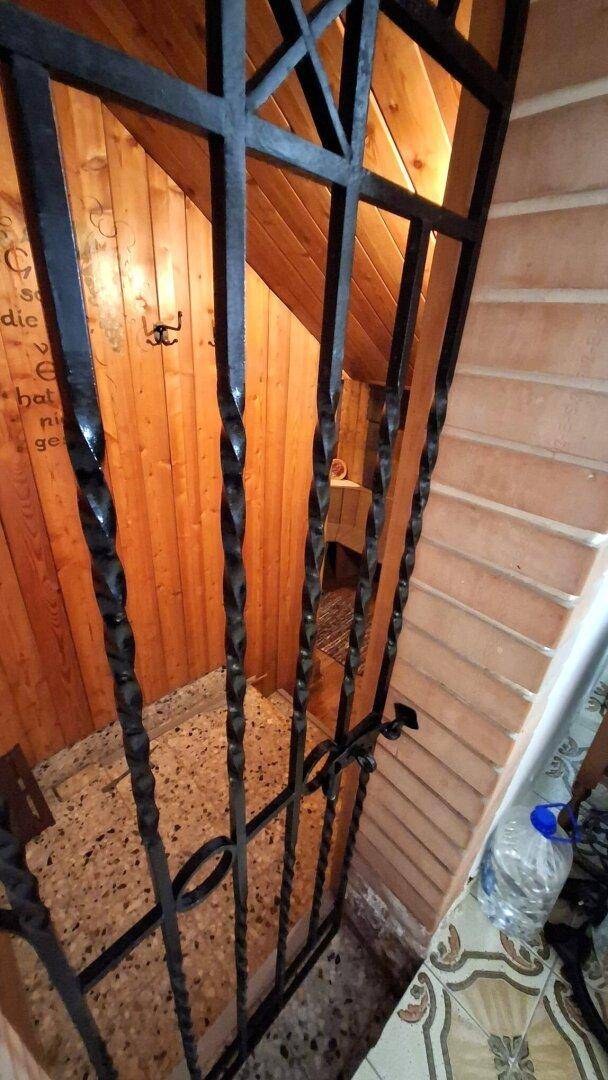 Blick auf eine Treppe mit schmiedeeisernem Gitter und Holzverkleidung an der Wand.