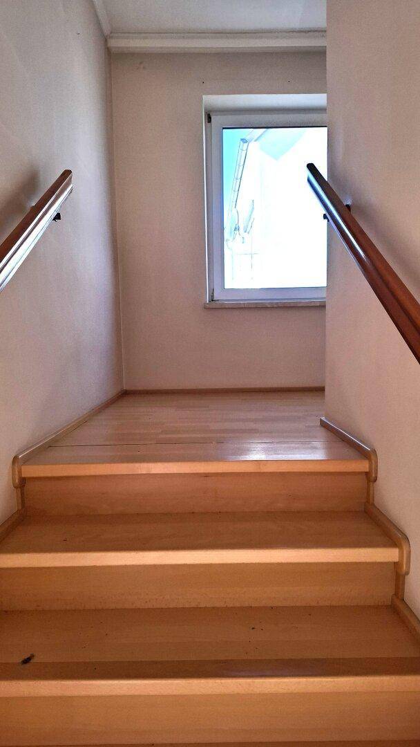 Helle Holztreppe mit Fenster am Treppenabsatz, die in die oberen Stockwerke führt.
