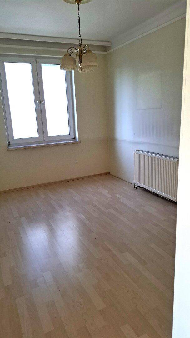 Helles Wohnzimmer mit Laminatboden, großem Fenster und Heizkörper.
