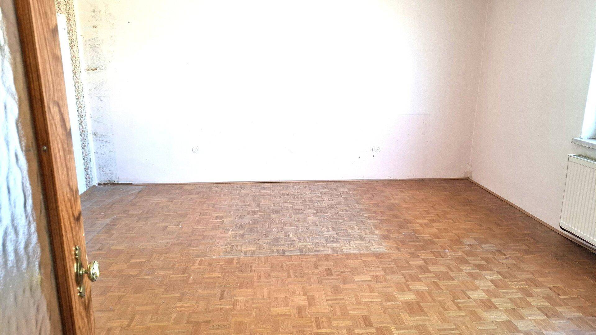 Geräumiges Wohnzimmer mit Parkettboden, Fenster und Heizkörper.