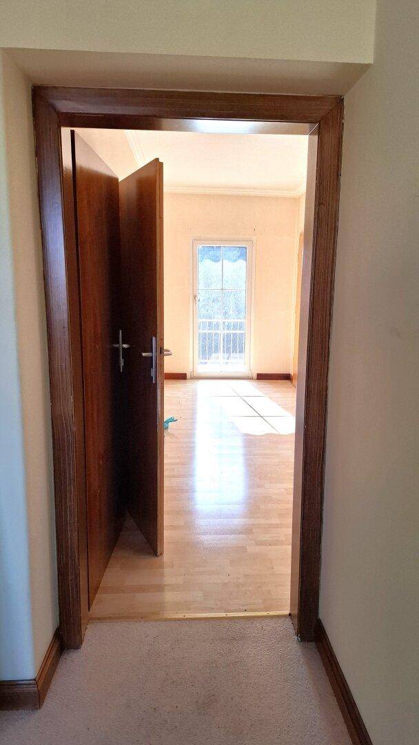 Blick durch eine Tür in ein helles Zimmer mit Laminatboden und französischem Balkon.