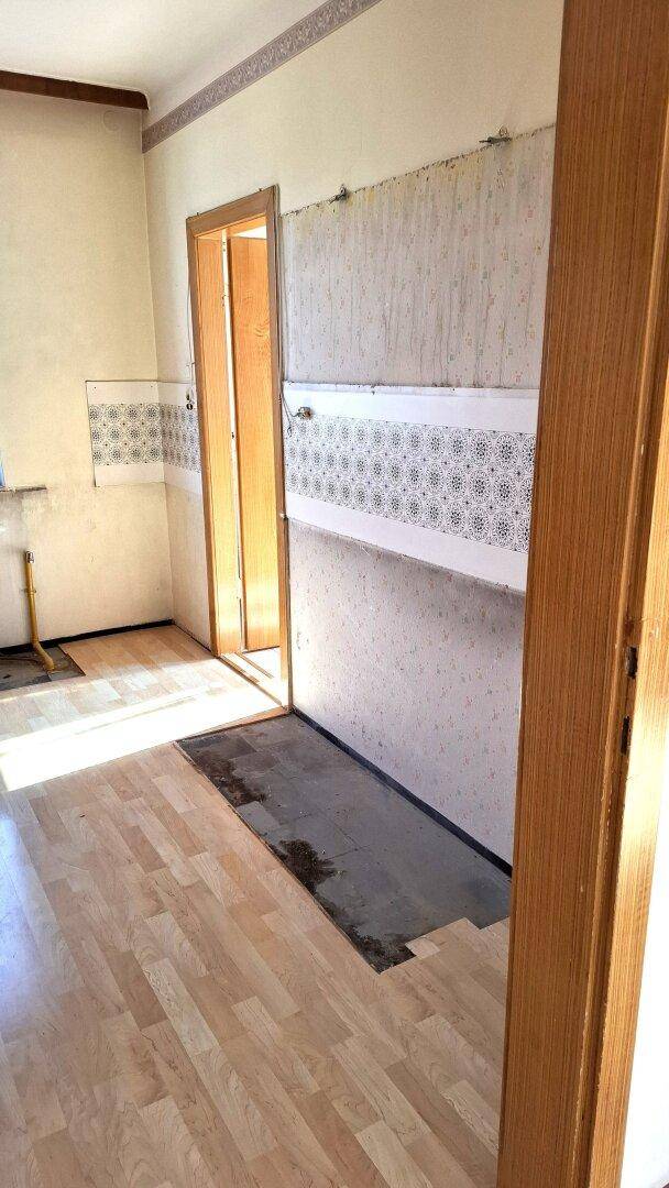 Küche mit Laminatboden und teilweise gefliesten Wänden, die renovierungsbedürftig ist.