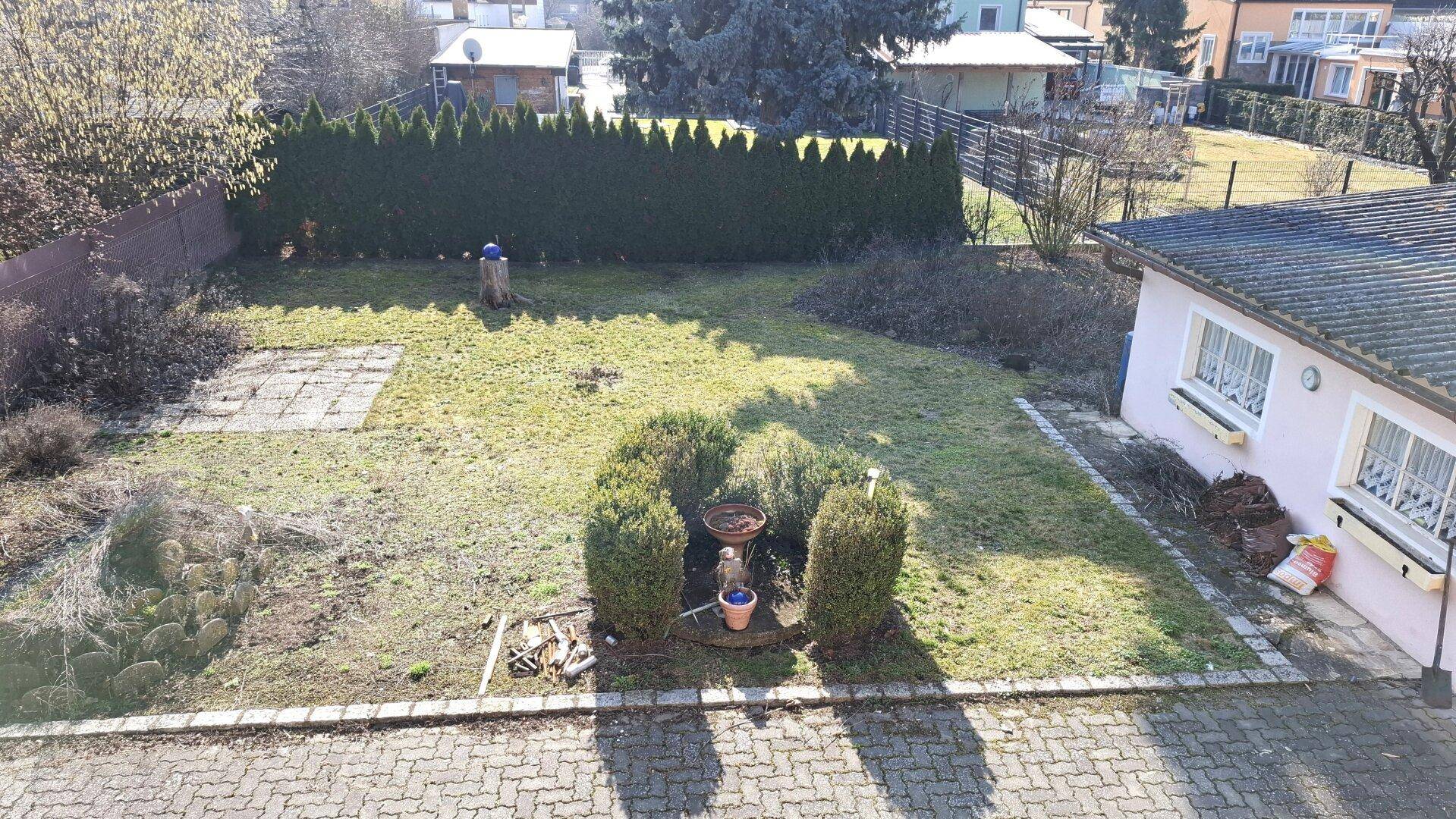 Blick von oben auf den Garten mit Rasenfläche, Sträuchern und Nebengebäude.