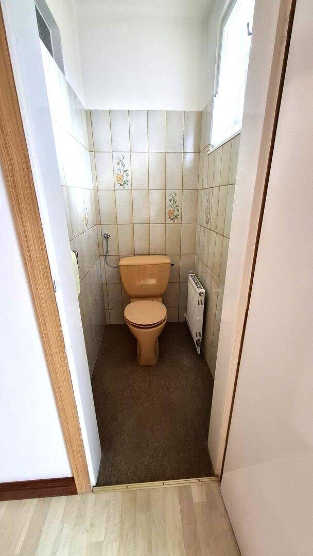 Kleines WC mit beigefarbener Toilette, gefliesten Wänden und kleinem Fenster.