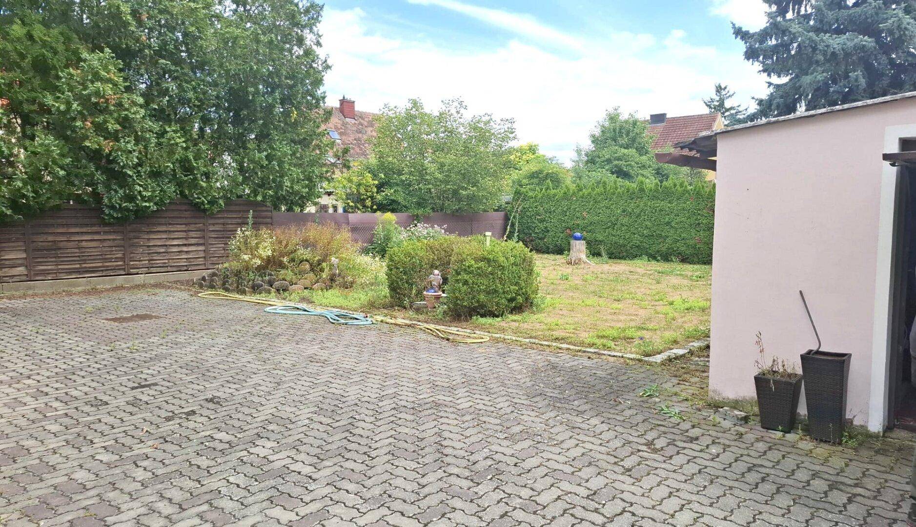 Gepflasterter Bereich im Hinterhof neben einem Nebengebäude und dem Garten.