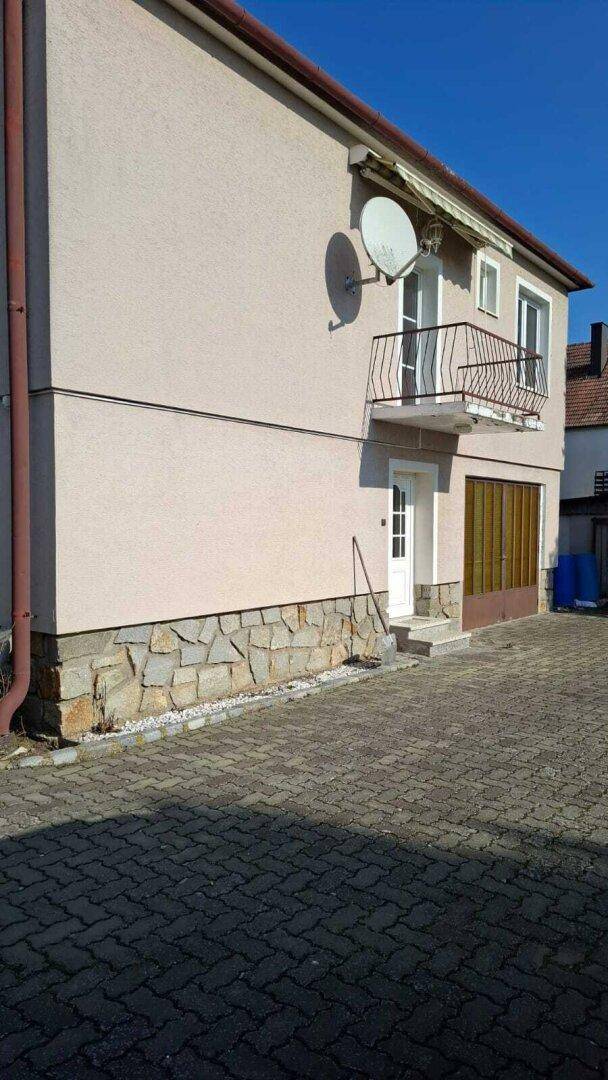 Seitenansicht des Hauses mit kleinem Balkon, Garagentor und Steinfassade im Sockelbereich.