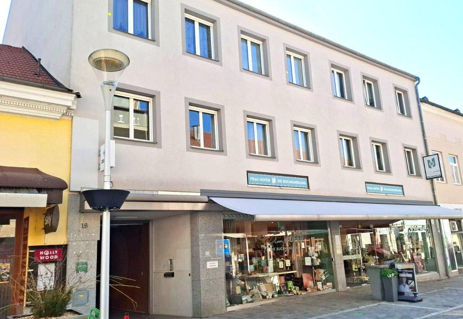 Ansicht der Gebäudefassade mit Geschäften im Erdgeschoss und Wohnungen darüber in städtischer Umgebung.