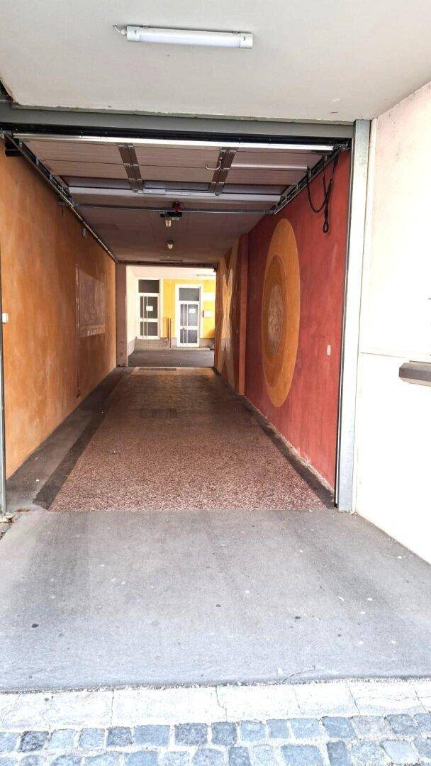 Überdachte Zufahrt oder Durchgang mit farbigen Wänden, der zu einem Innenhof führt.