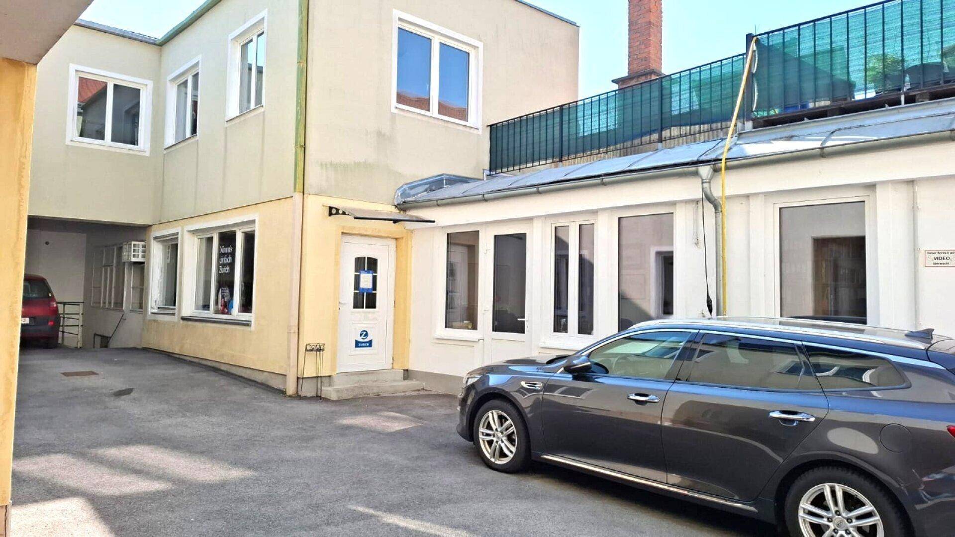 Hinterhof mit geparktem Auto, Gebäudefassaden und einem Eingangsbereich.