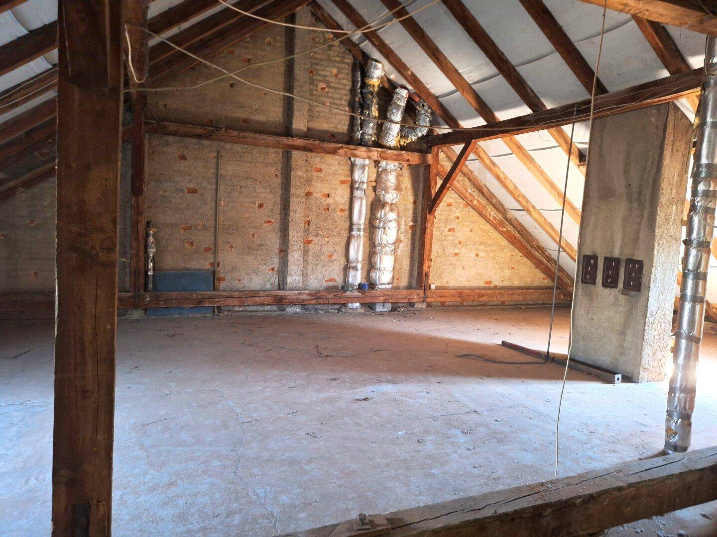 Geräumiger, unausgebauter Dachboden mit sichtbaren Holzbalken und Ziegelwänden.