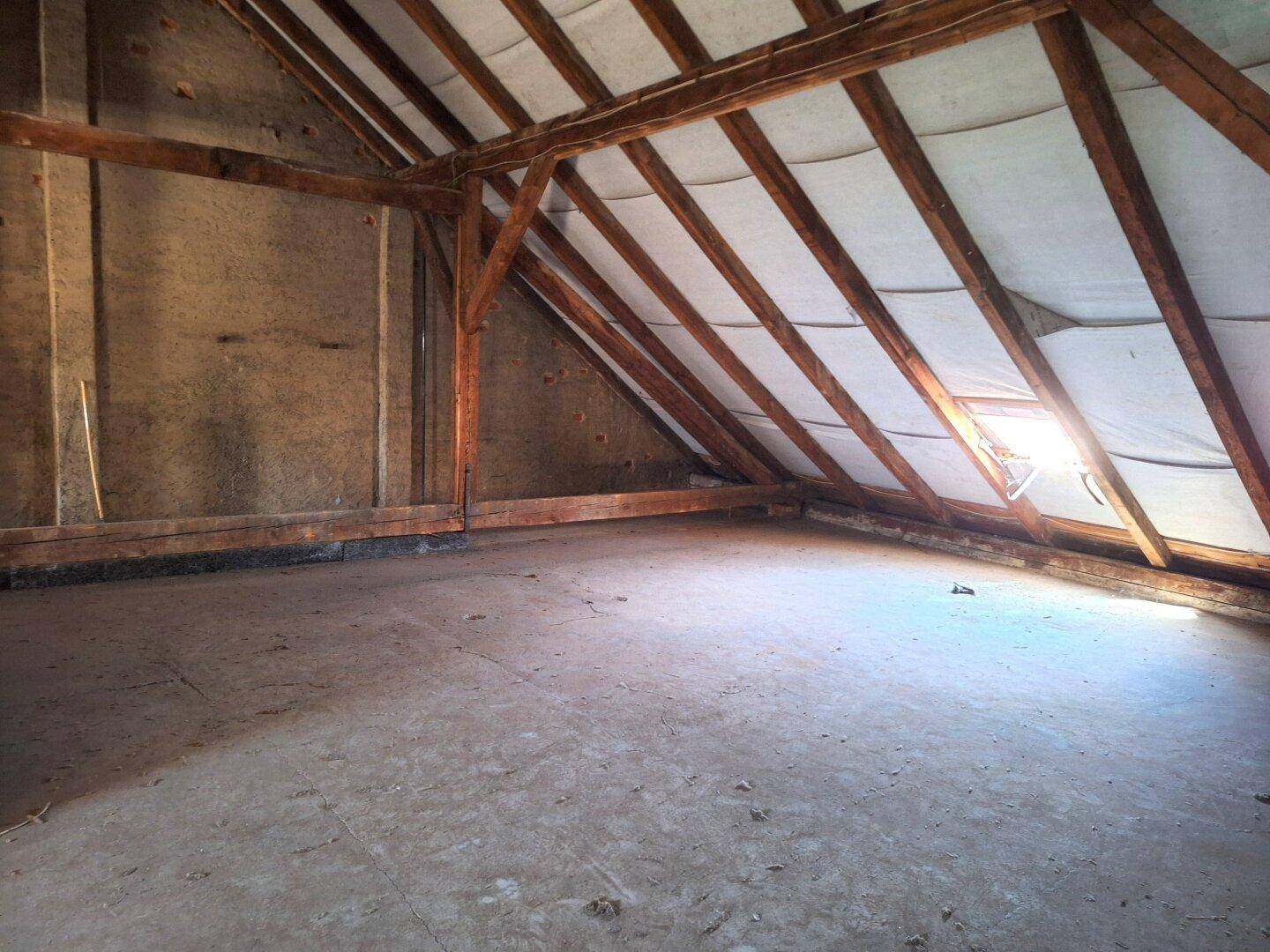 Unausgebauter Dachboden mit Holzdachstuhl und einem Dachfenster für natürliches Licht.