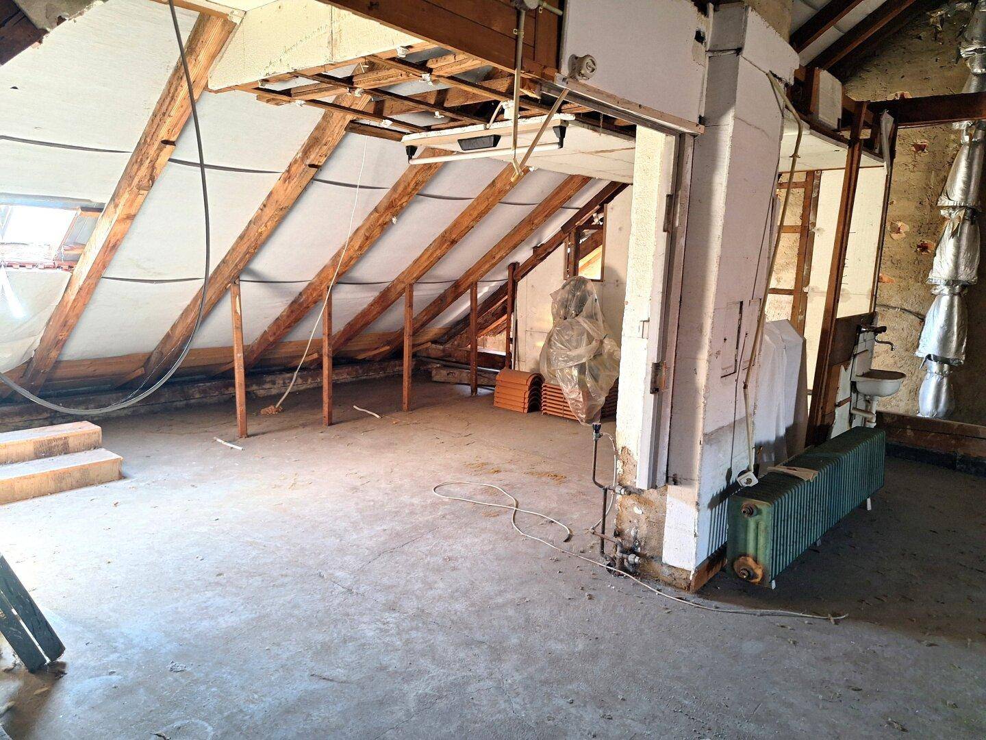Dachboden mit sichtbaren Holzbalken, alten Heizkörpern und Potenzial zum Ausbau.