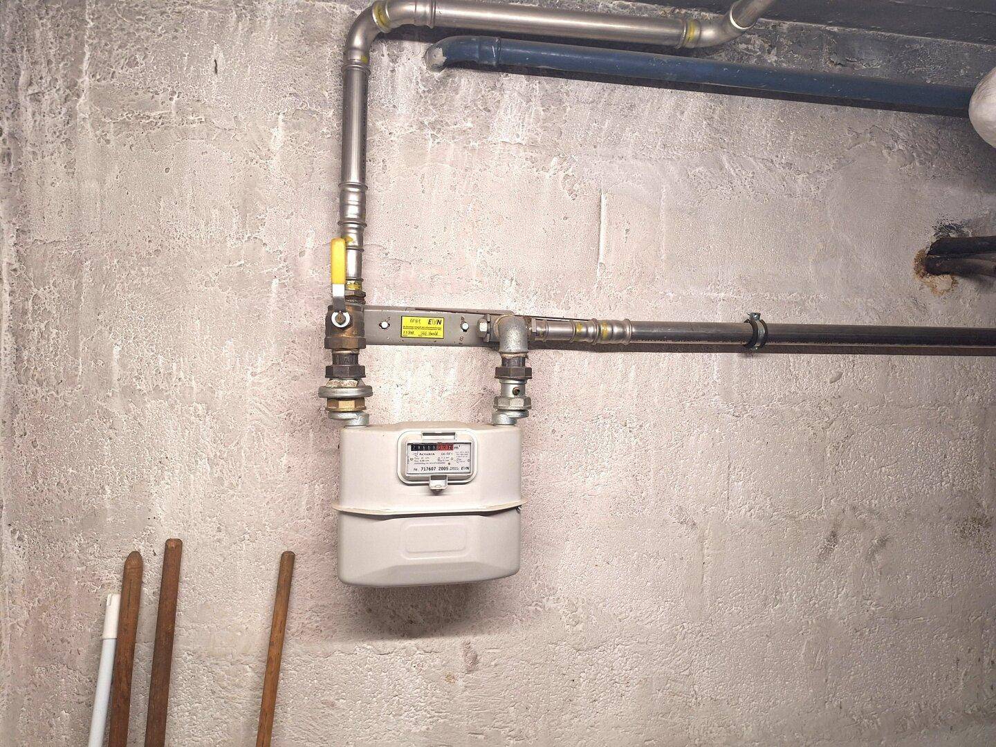 Gaszähler und Rohrleitungen an einer Betonwand im Kellerbereich.
