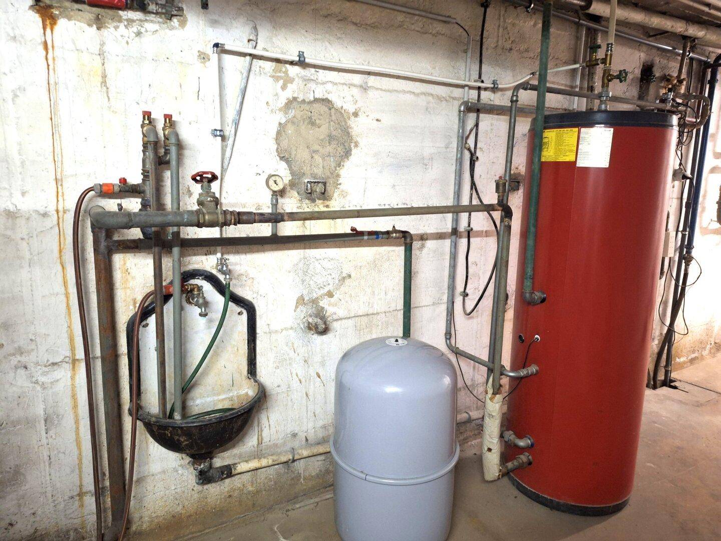 Warmwasserspeicher und Rohrinstallationen in einem Versorgungsraum im Keller.