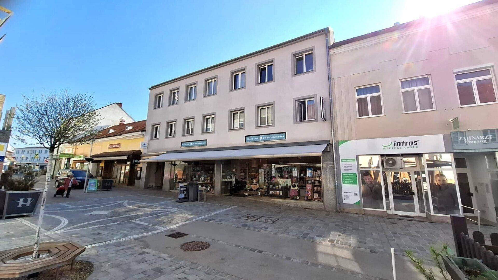 Weitwinkelansicht der Gebäudefassade mit Geschäften und Wohnungen an einer belebten Straße.