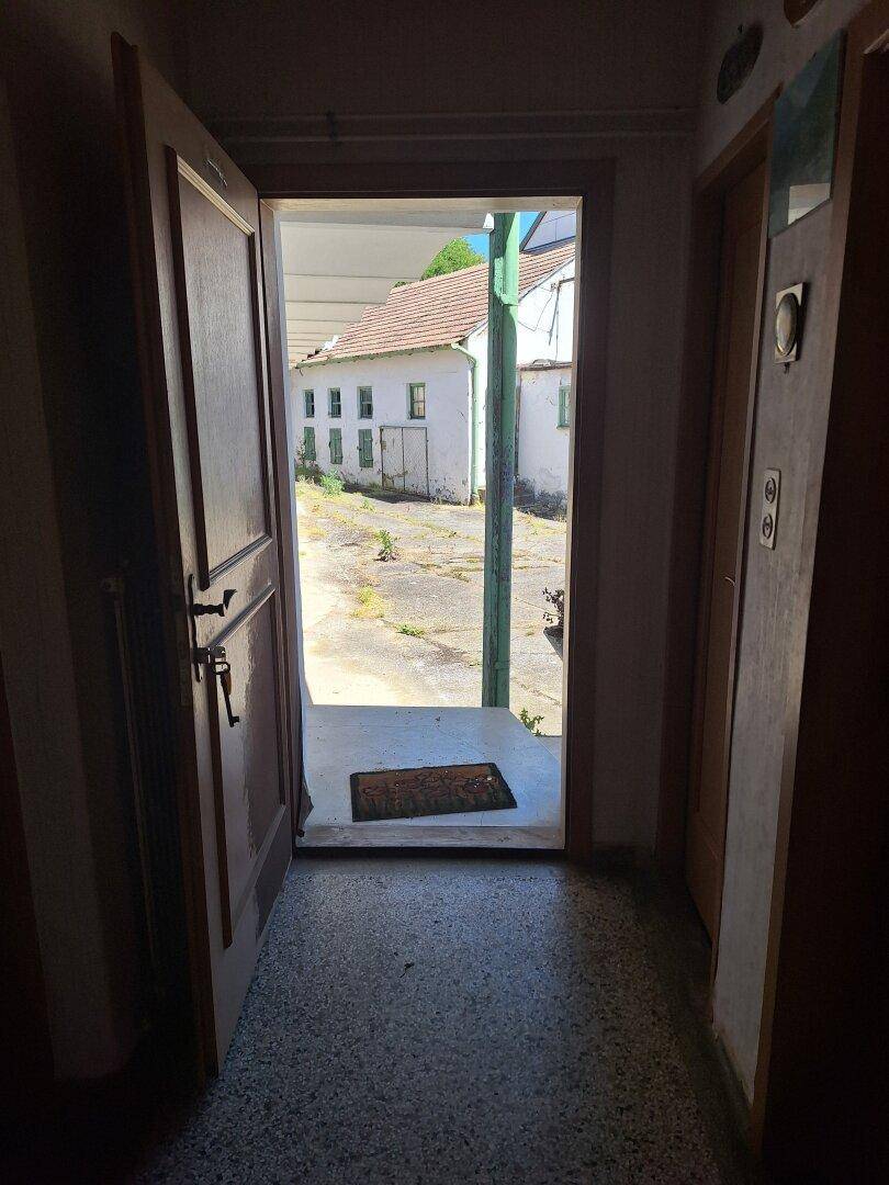 Blick aus einem dunklen Flur durch eine offene Tür auf den sonnigen Innenhof.