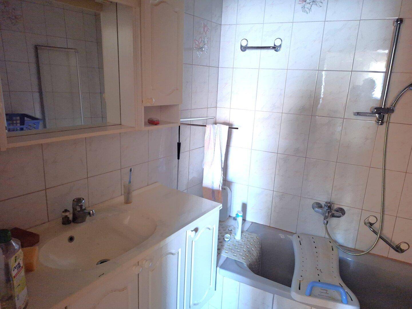 Badezimmer mit weißen Fliesen, einem Waschbecken und einer Badewanne mit Duschvorrichtung.