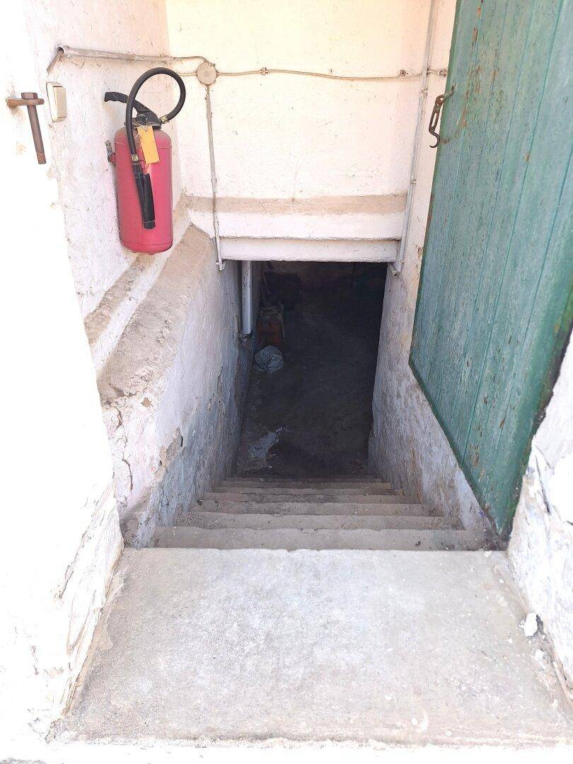 Eingang zum Keller mit Betontreppe und einem Feuerlöscher an der Wand.