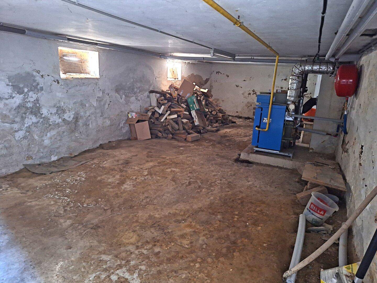 Kellerraum mit einem Heizsystem, Holzstapeln und unfertigen Wänden.