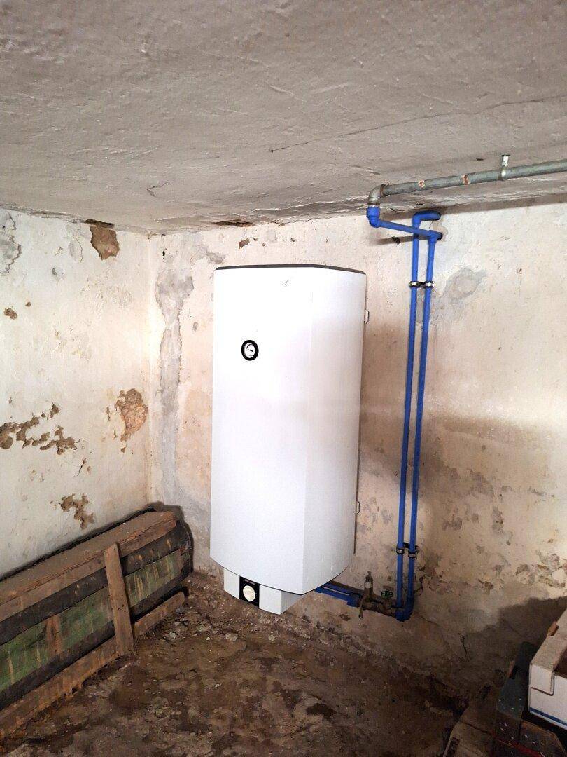 Neuer Warmwasserspeicher in einem rustikalen Kellerraum mit unverputzten Wänden und sichtbaren Rohren.