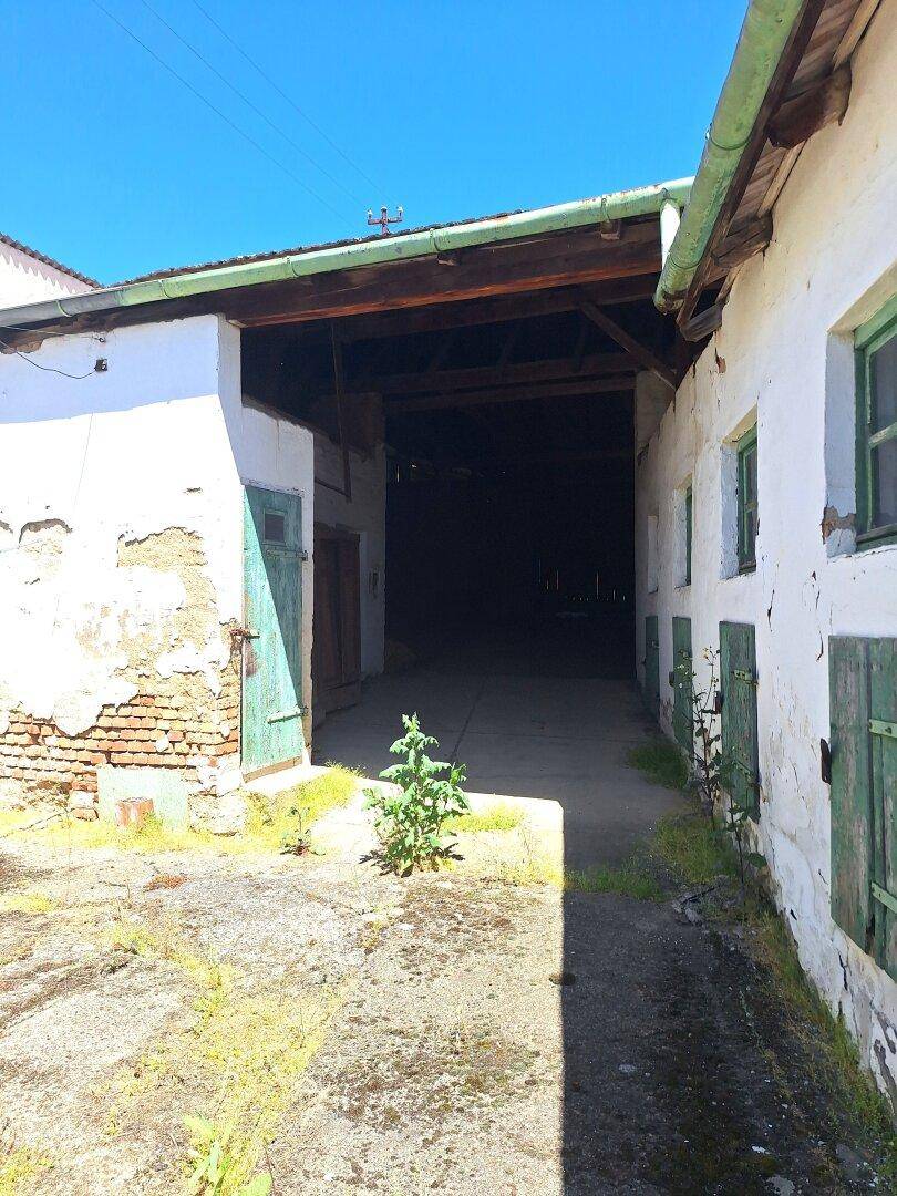 Altes Bauernhaus mit grünen Fensterläden und einem großen, dunklen Durchgang zum Innenhof.