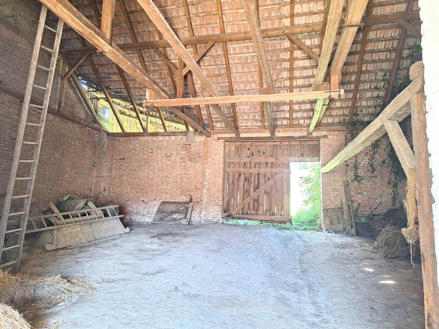 Geräumige Scheune mit hohen Holzbalkendecken, Ziegelwänden und großem Holztor.
