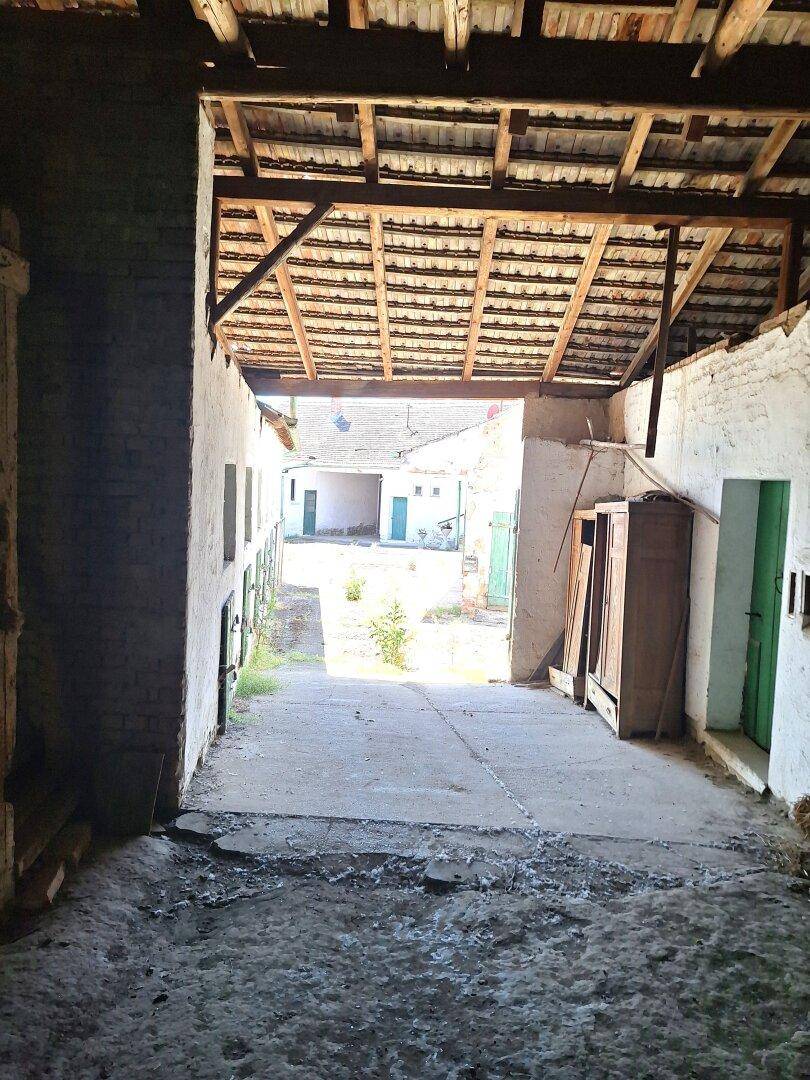 Blick durch einen überdachten Durchgang auf einen sonnigen Innenhof mit alten Gebäuden.