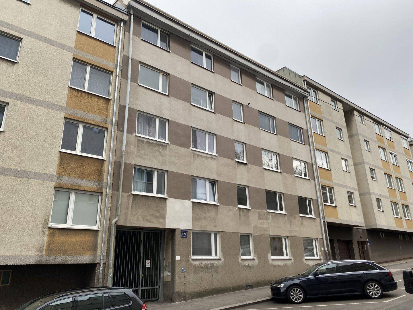 Mehrfamilienhaus mit mehreren Stockwerken und zahlreichen Fenstern an einer städtischen Straße.