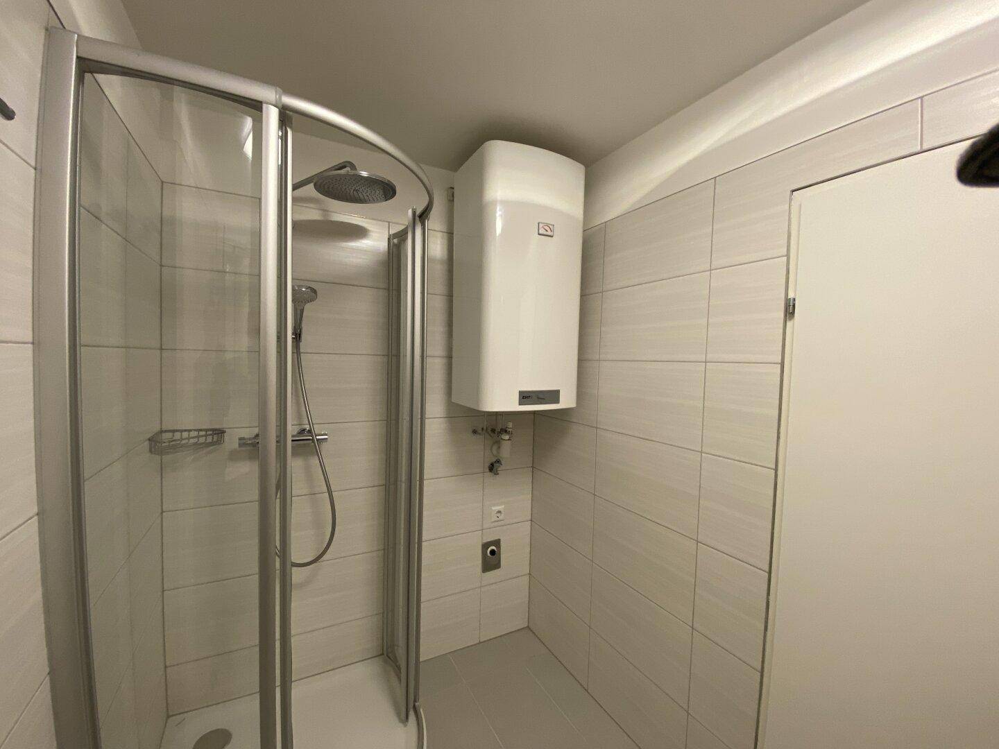 Modernes Badezimmer mit Duschkabine und weißem Warmwasserboiler an der gefliesten Wand.