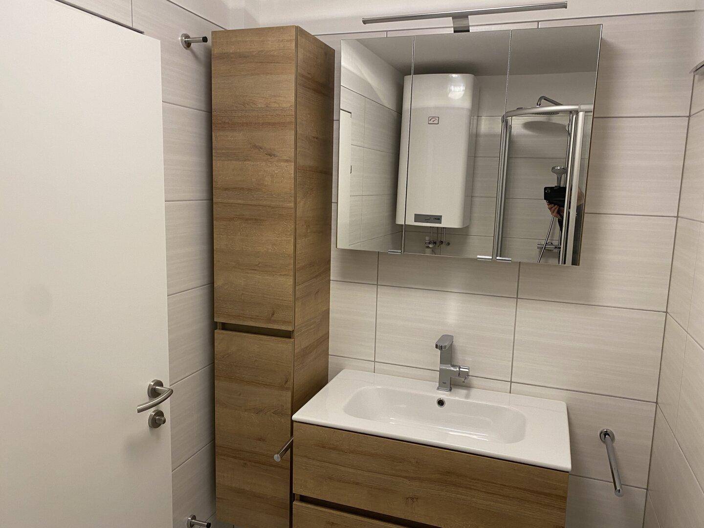 Badezimmer mit modernem Waschtisch, Spiegelschrank und hohem Holzschrank für zusätzlichen Stauraum.