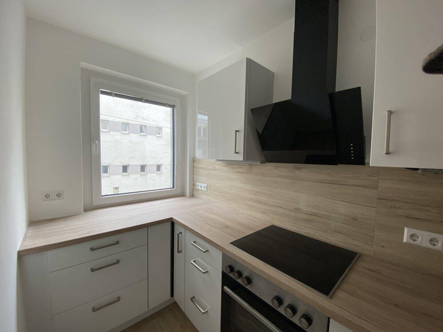 Moderne Küche mit weißen Schränken, Holz-Arbeitsplatten, Induktionskochfeld und Dunstabzugshaube.