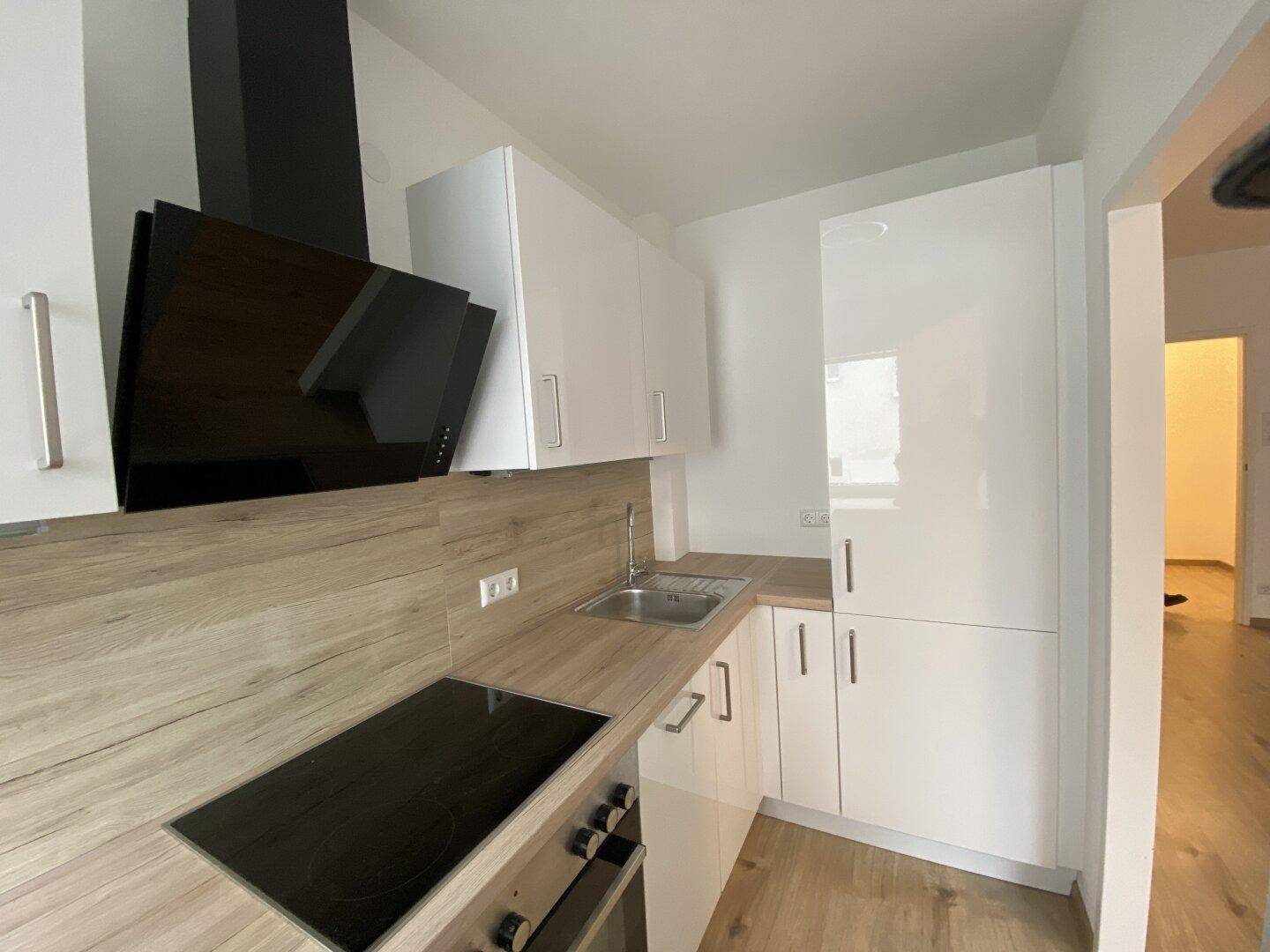 Helle Einbauküche mit glänzenden weißen Fronten, Holz-Arbeitsplatten und integriertem Spülbecken.