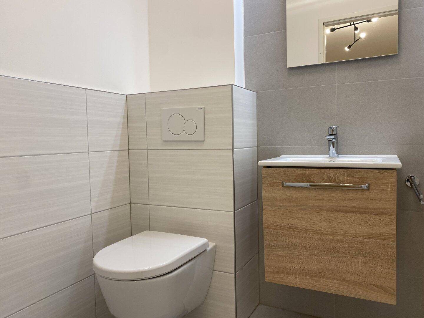Separates WC mit wandhängender Toilette, modernem Waschtisch und hellen Fliesen.
