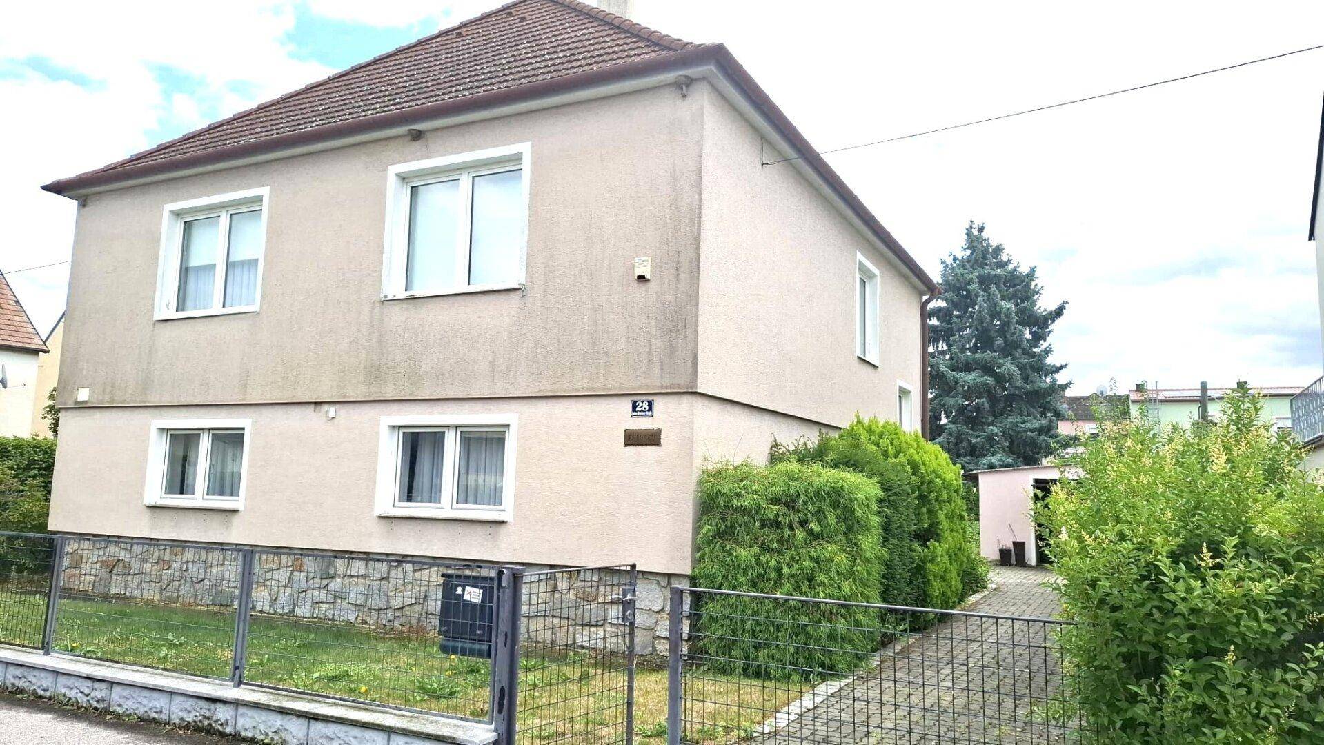 Vorderansicht des Hauses mit beiger Fassade, kleinem Vorgarten und einem Metallzaun.