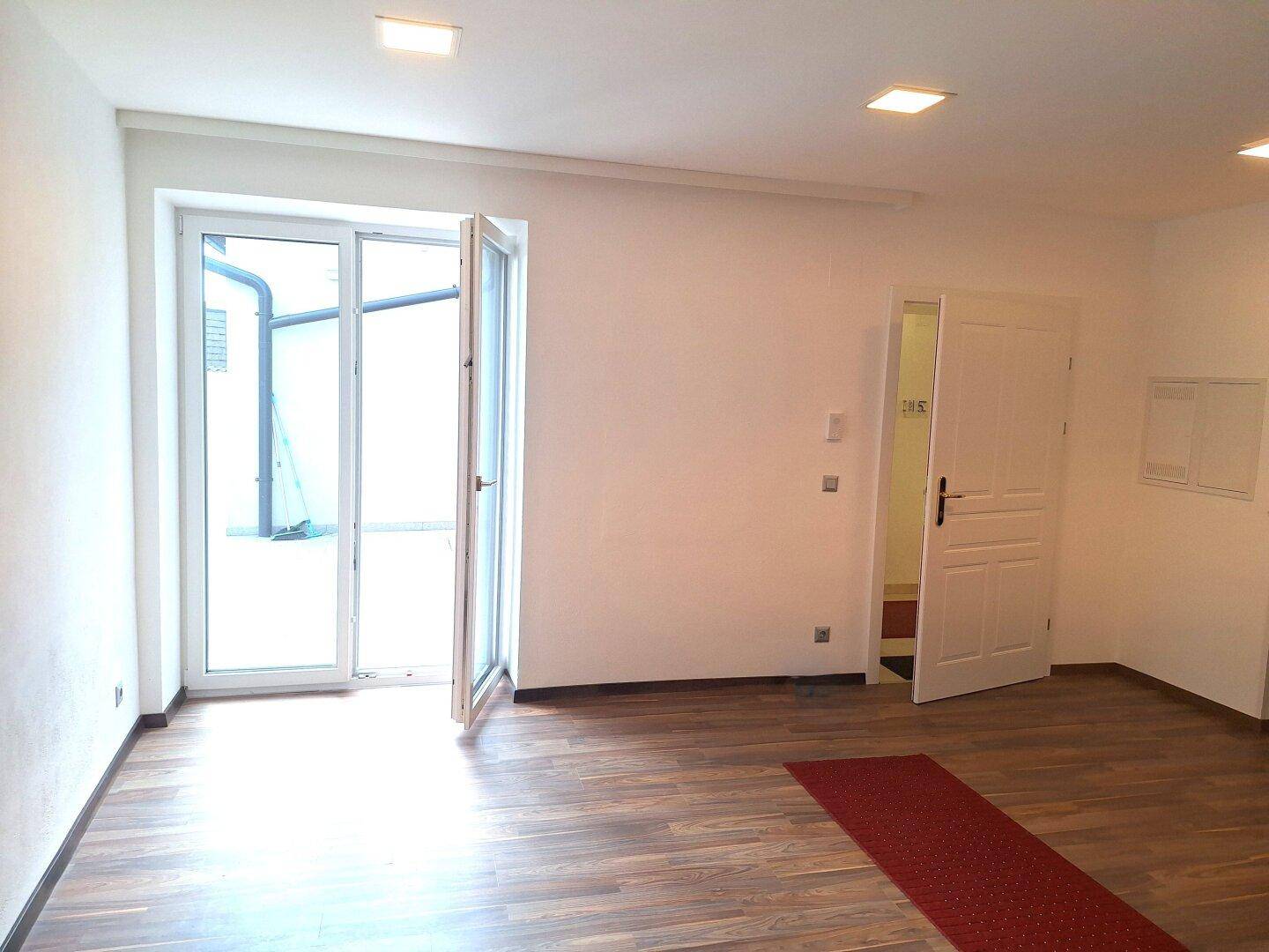 Heller Raum mit Holzboden und Zugang zu einem Außenbereich, ideal für verschiedene Nutzungen.