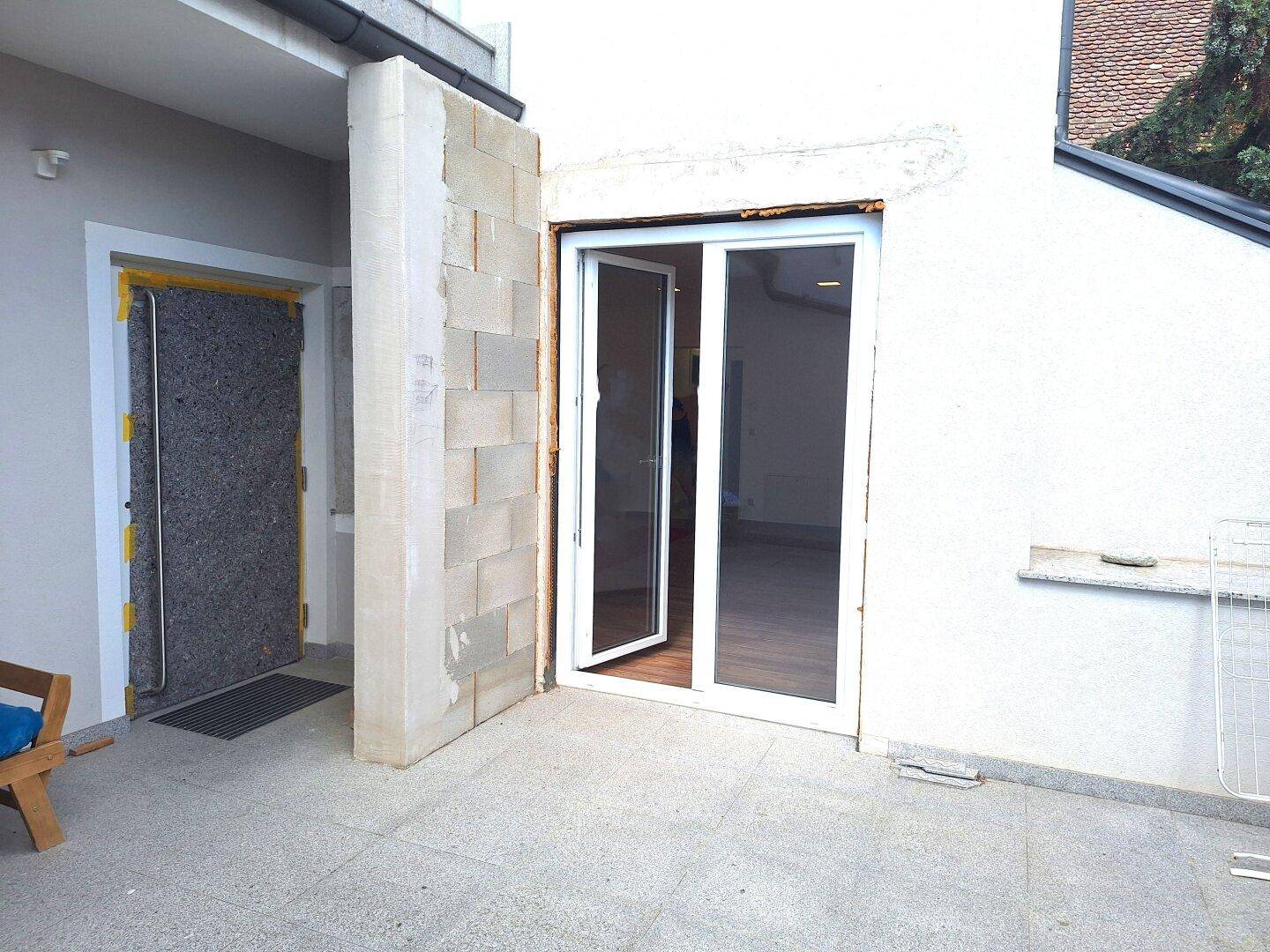 Terrasse mit Betonplatten und Zugang zu einem Innenraum, umgeben von Rohbauwänden.