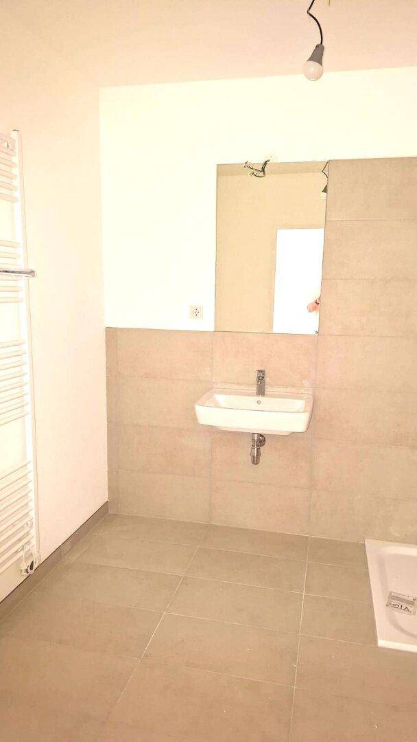 Modernes Badezimmer mit Waschbecken, Spiegel und beigefarbenen Fliesen an Wänden und Boden.