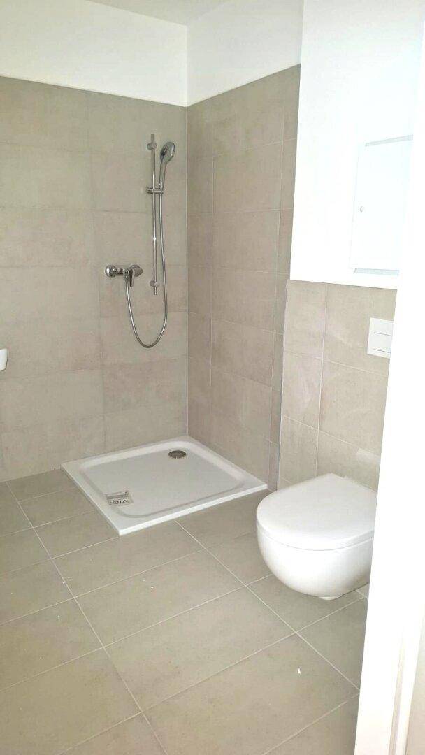 Modernes Badezimmer mit ebenerdiger Dusche und wandhängendem WC, ausgestattet mit beigefarbenen Fliesen.