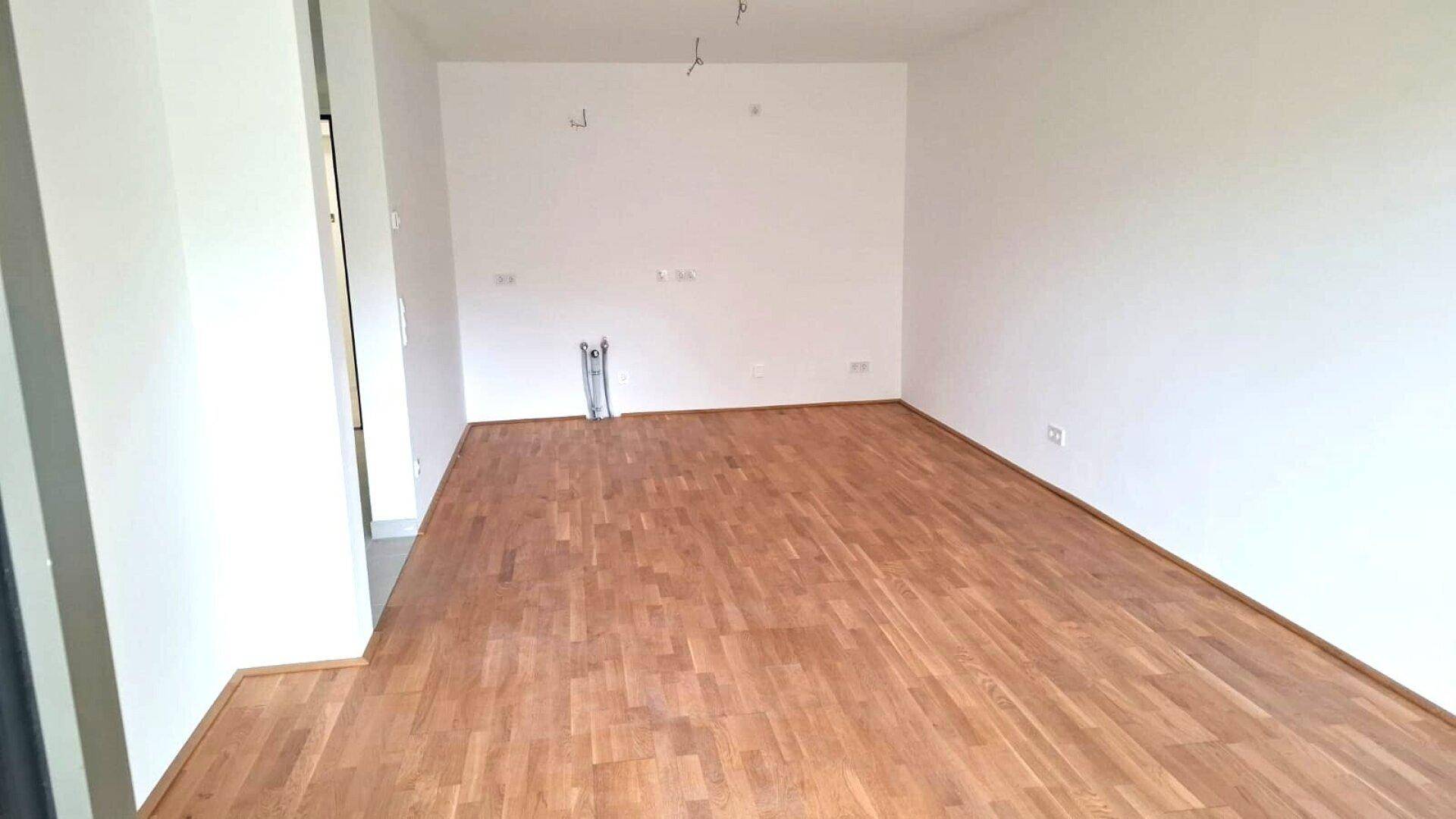 Geräumiges Wohnzimmer mit hellem Parkettboden und Anschlüssen für eine zukünftige Küche.