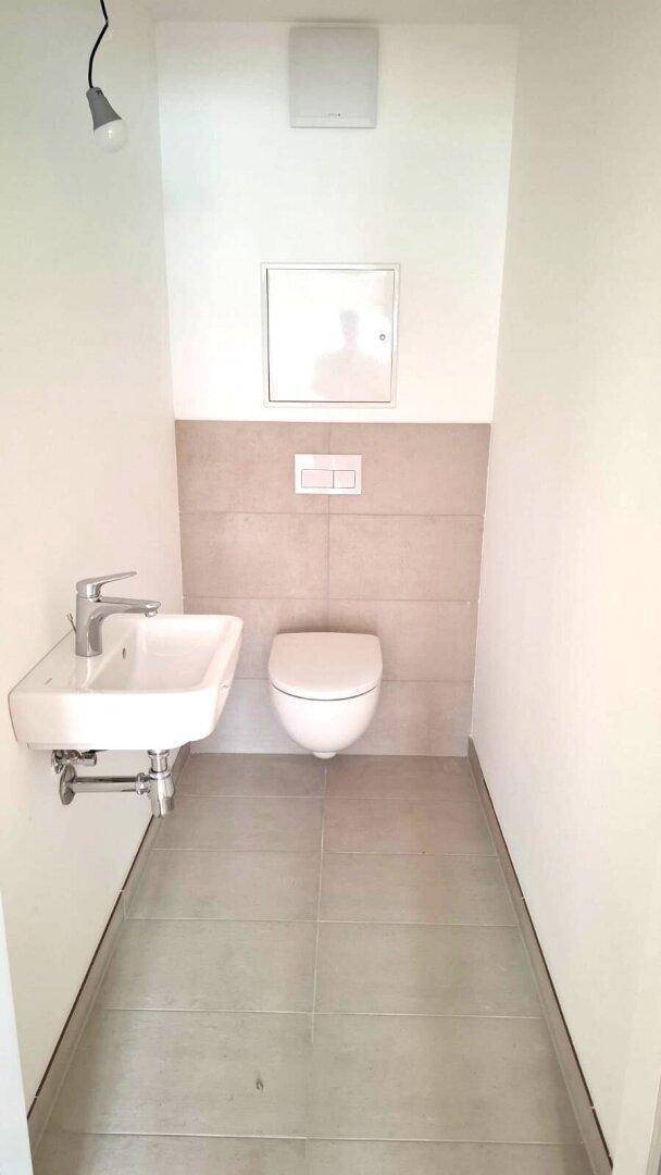 Kleines Gäste-WC mit wandhängendem WC und Waschbecken, ausgestattet mit beigefarbenen Fliesen.